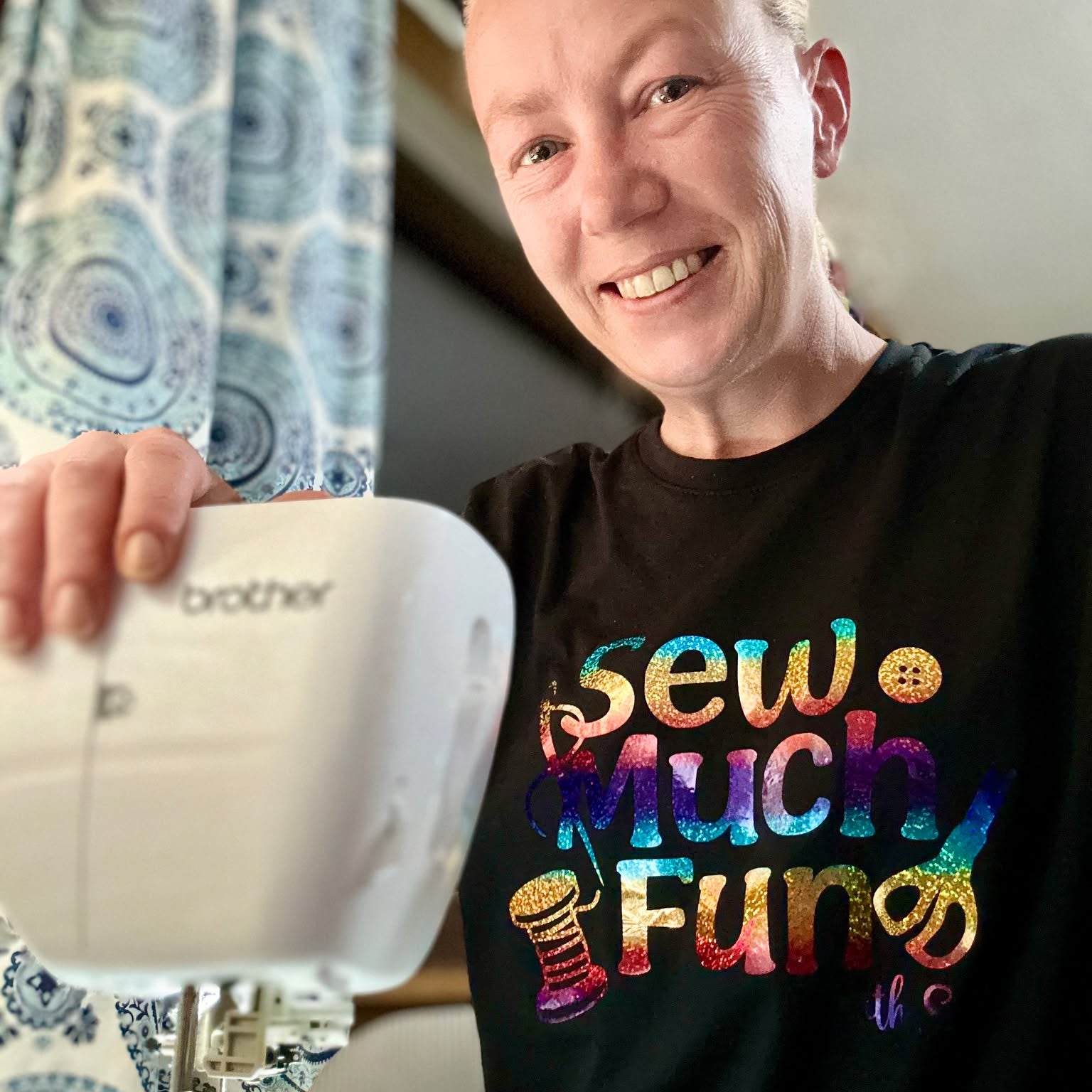 Person wearing a black t-shirt with colorful text, using a Brother sewing machine.
